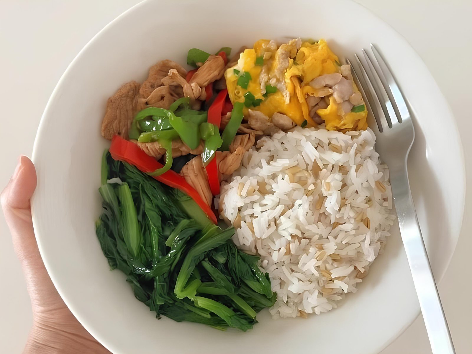 Sepiring makanan sehat terdiri dari nasi campur, sayuran hijau, ayam, paprika, dan telur orak-arik.